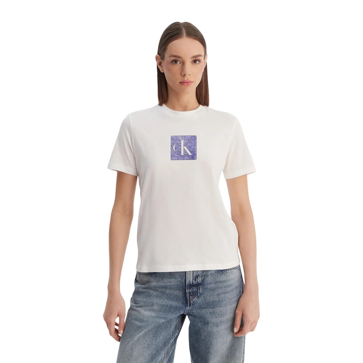 Image 1 : Femme portant le t-shirt blanc Calvin Klein Jeans avec logo CK carré texturé violet au centre, coupe ajustée, encolure ronde, porté avec un jean clair — Delvale