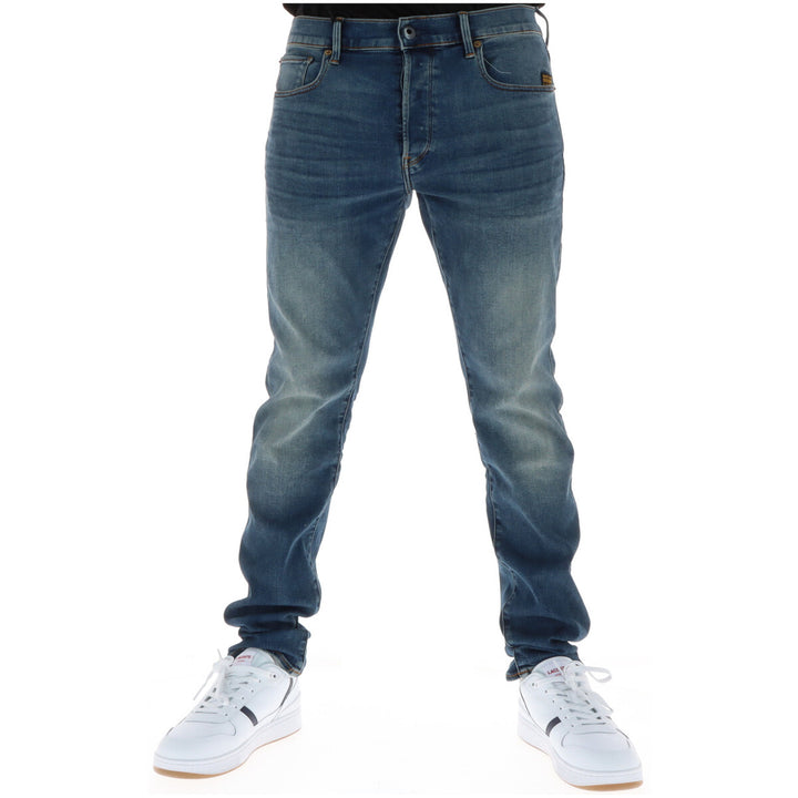 Image 1 : Jean slim G-Star homme en denim bleu effet usé porté avec des sneakers blanches Lacoste, vue frontale — Delvale