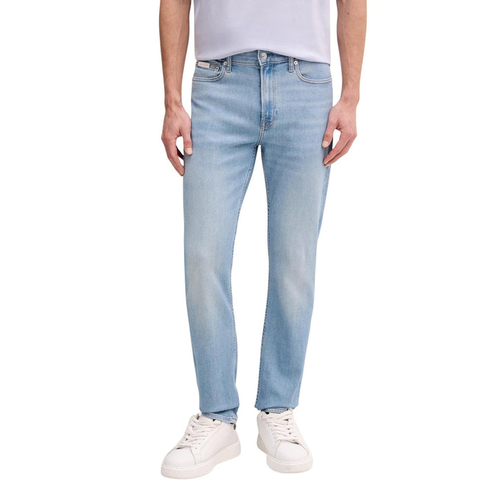 Image 1 : Jean droit Calvin Klein Jeans homme en denim bleu clair, coupe straight, porté avec un t-shirt lavande et des sneakers blanches — Delvale