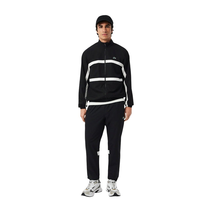 Image 1 : Survêtement Lacoste homme noir avec bandes blanches contrastées, veste zippée col montant et pantalon jogging assortis, vue de face — Delvale