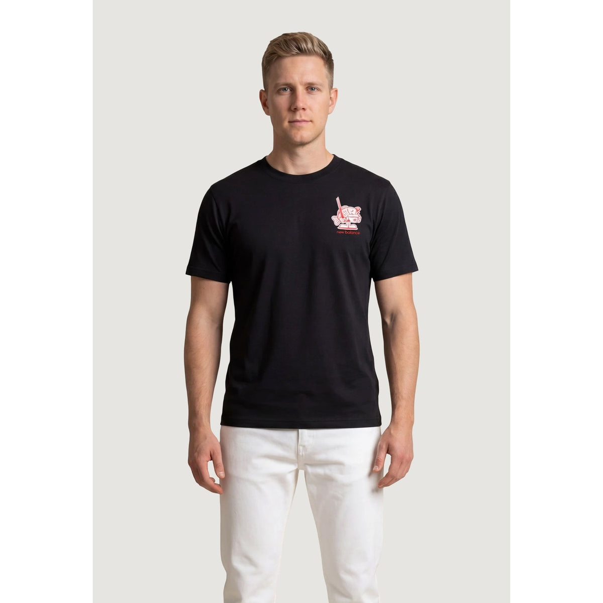 Image 1 : T-shirt New Balance homme noir à col rond avec imprimé graphique rouge et blanc sur la poitrine, porté par un homme aux cheveux blonds sur fond blanc — Delvale