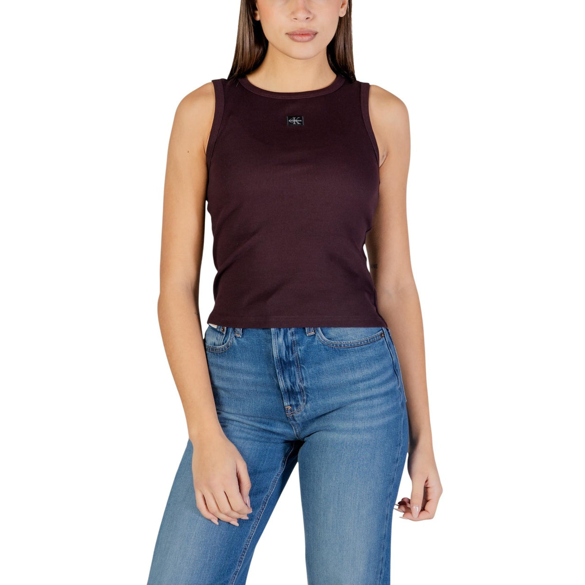 Image 1 : Femme portant un débardeur côtelé bordeaux Calvin Klein Jeans avec badge logo CK centré, associé à un jean brut — Delvale
