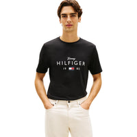 Image 1 : T-shirt noir Tommy Hilfiger Jeans homme avec logo signature imprimé en blanc sur la poitrine, porté par un homme brun sur fond blanc — Delvale
