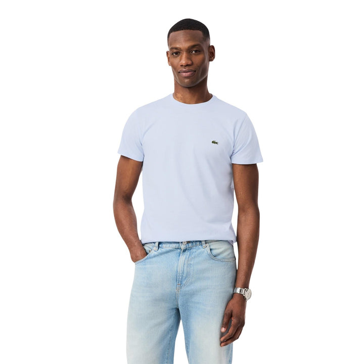 Image 1 : Homme portant un t-shirt Lacoste bleu azur à col rond avec crocodile brodé vert, associé à un jean clair — Delvale