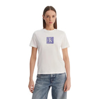 Image 1 : Femme portant le t-shirt blanc Calvin Klein Jeans avec logo CK carré texturé violet au centre, coupe ajustée, encolure ronde, porté avec un jean clair — Delvale