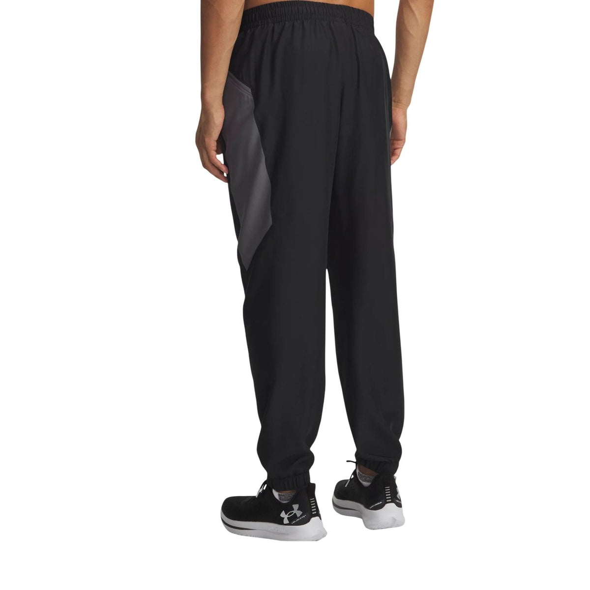 Pantalon technique Under Armour homme noir et gris porté de dos, insert contrasté gris sur les hanches, chevilles élastiquées