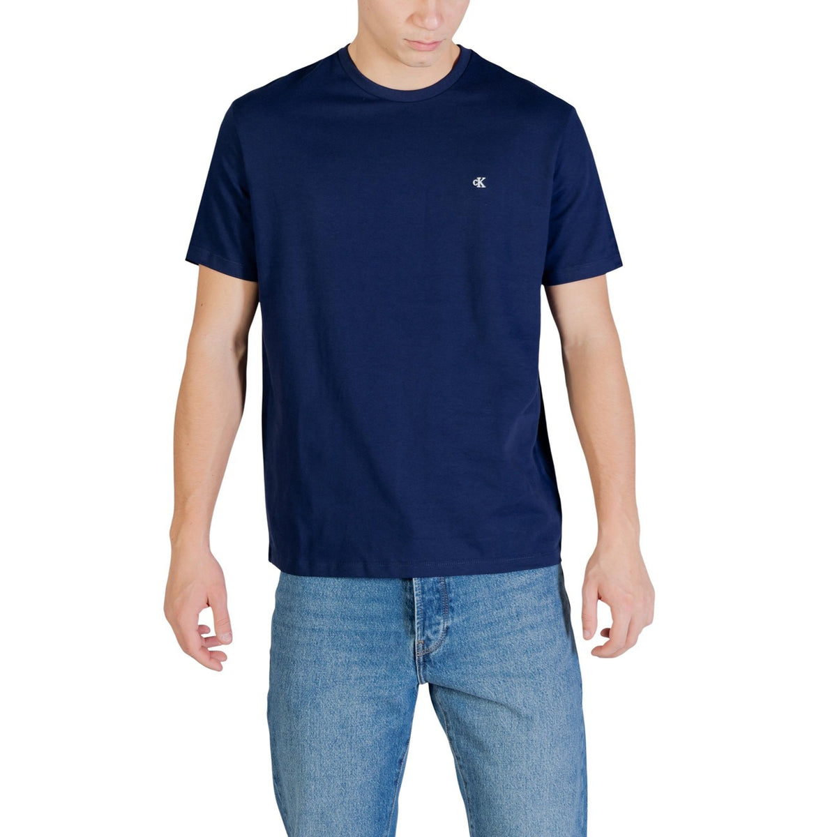 Image 1 : T-shirt homme Calvin Klein Jeans bleu marine uni avec logo CK brodé sur la poitrine, porté avec un jean brut, vue de face — Delvale