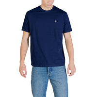 Image 1 : T-shirt homme Calvin Klein Jeans bleu marine uni avec logo CK brodé sur la poitrine, porté avec un jean brut, vue de face — Delvale