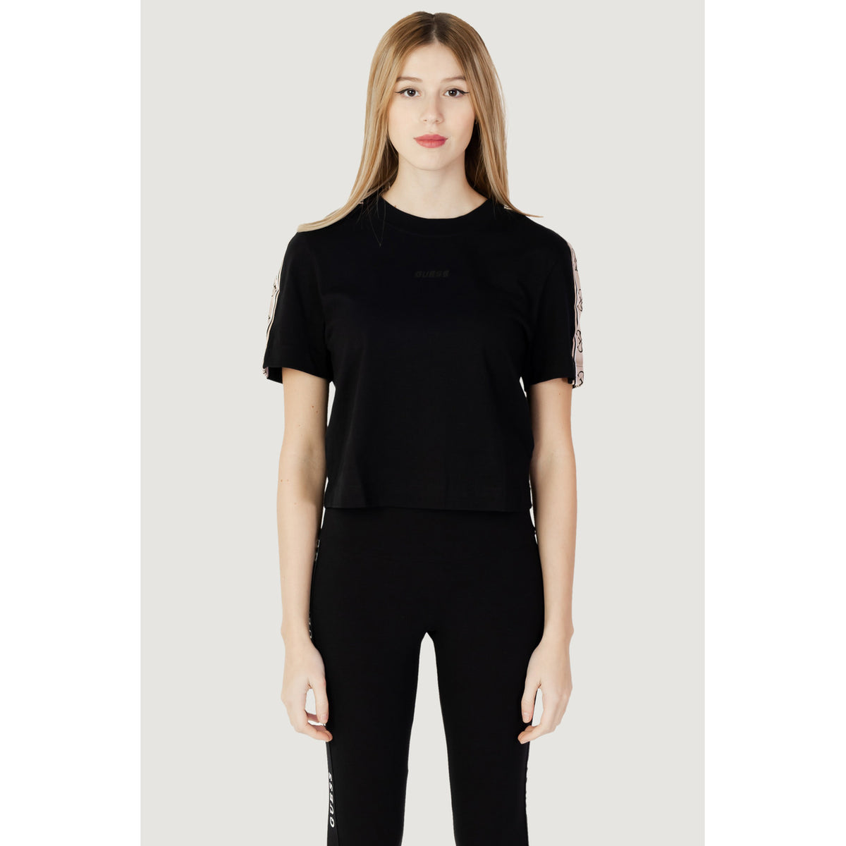 T-shirt crop Guess Active femme noir de face, bandes monogramme beige rosé aux épaules, logo GUESS ton sur ton, coupe carrée courte