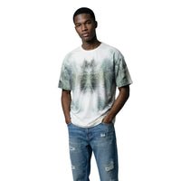 Image 1 : Homme portant le t-shirt Antony Morato blanc à imprimé palmier all-over en camaïeu vert, coupe oversize, col rond, manches courtes, associé à un jean déchiré bleu — Delvale