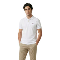 Image 1 : Homme portant le polo piqué Gant blanc avec logo Shield brodé, col polo deux boutons et manches courtes, associé à un pantalon chino beige — Delvale