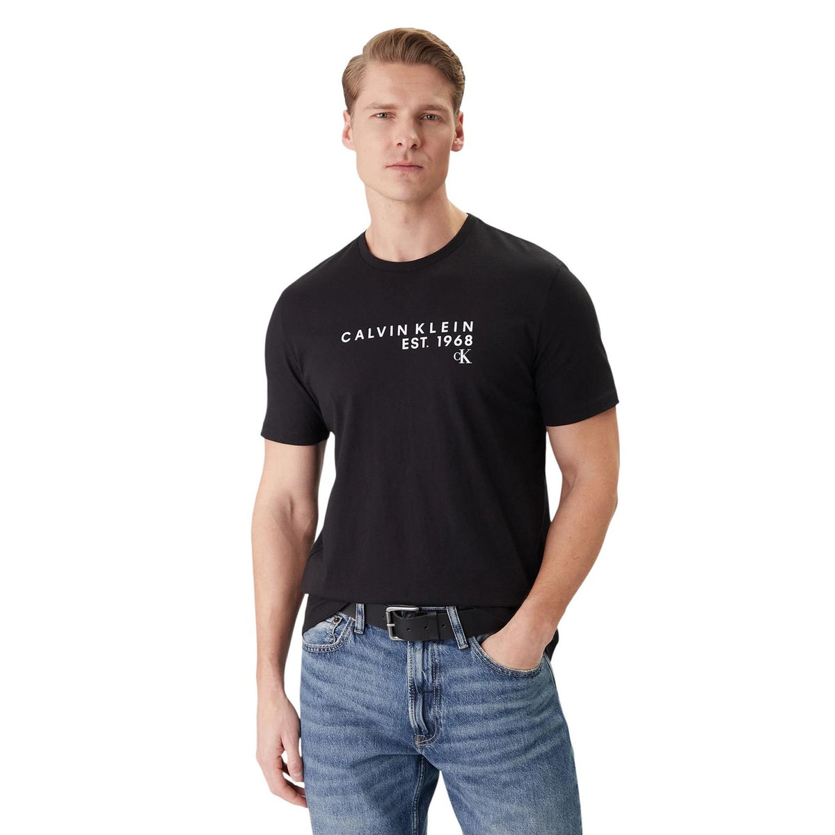 Image 1 : Homme portant le t-shirt Calvin Klein noir à logo Est. 1968 blanc, col rond, manches courtes, associé à un jean clair et une ceinture noire — Delvale