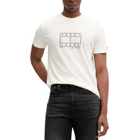 Image 1 : T-shirt Tommy Hilfiger Jeans homme écru avec logo flag graphique 'Tommy Jeans N.Y.C. 1985' imprimé au centre poitrine, porté avec un jean noir — Delvale