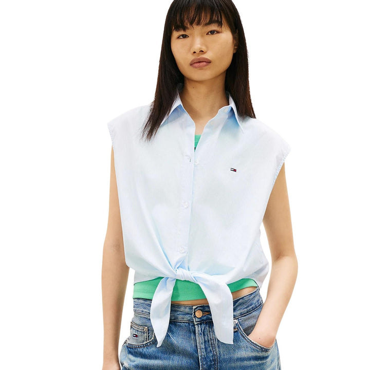 Image 1 : Chemise sans manches Tommy Hilfiger Jeans femme en coton bleu azur, col classique et fermeture boutonnée, portée nouée à la taille sur un jean — Delvale