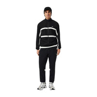 Image 1 : Survêtement Lacoste homme noir avec bandes blanches contrastées, veste zippée col montant et pantalon jogging assortis, vue de face — Delvale
