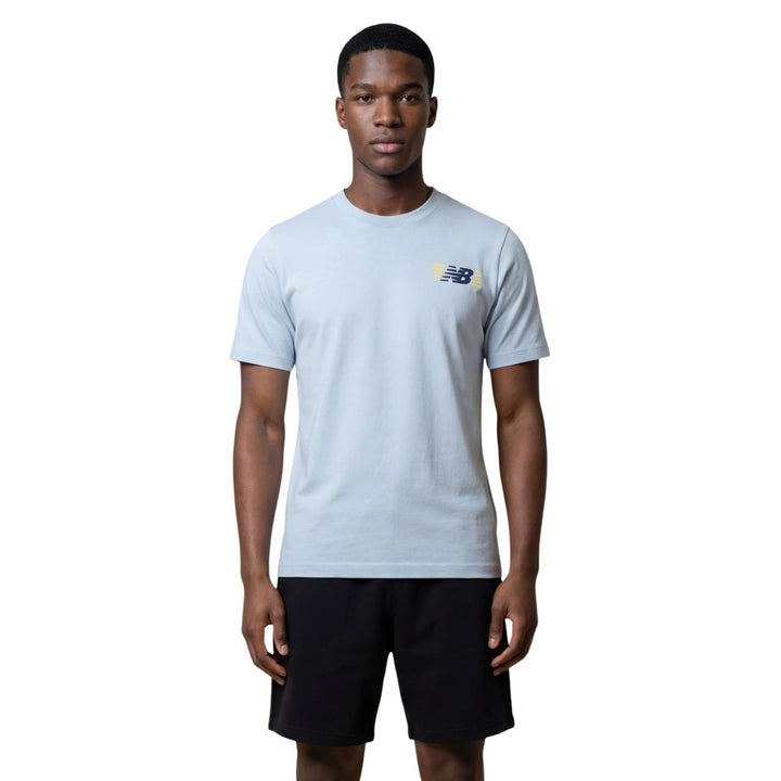 Image 1 : T-shirt homme New Balance bleu azur à col rond avec logo NB bicolore marine et jaune pâle sur la poitrine gauche, porté par un homme — Delvale
